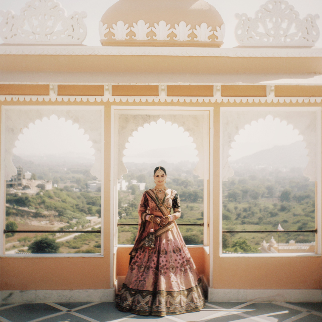 A bride in a red lehenga standing in a palace archway