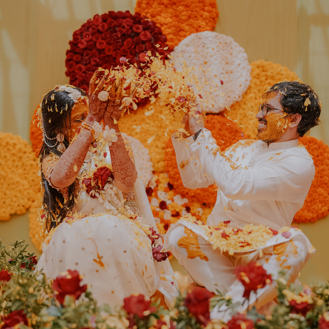 A couple laughing as family smear them with turmeric at their Haldi