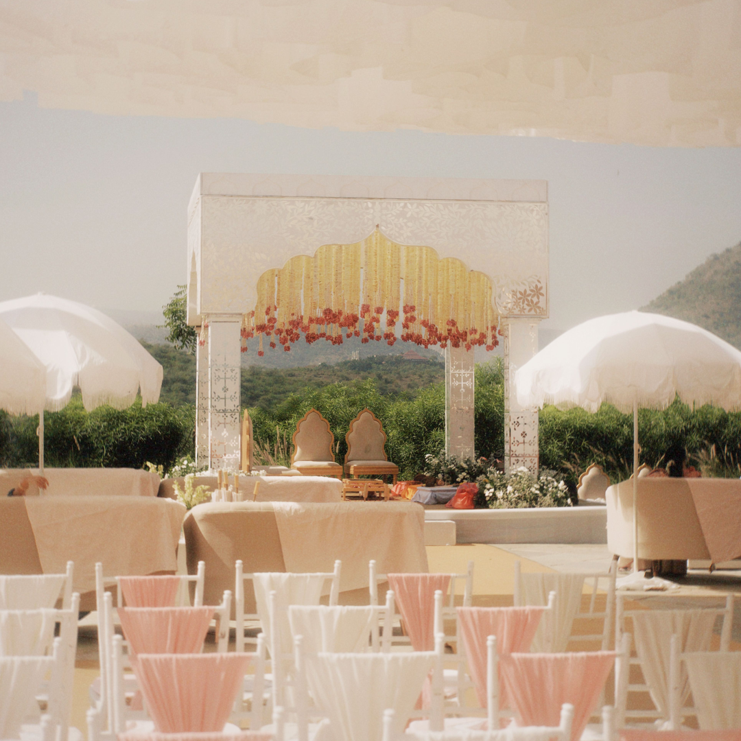 Reception tables and chairs set up outdoors in front of a floral mandap