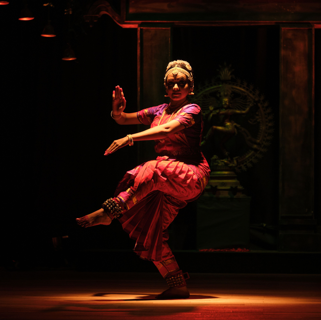 A Bharatanatyam dancer performing on a dimly lit stage